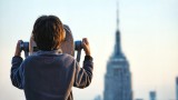 a child looks through a large telescope at the skyline of NYC