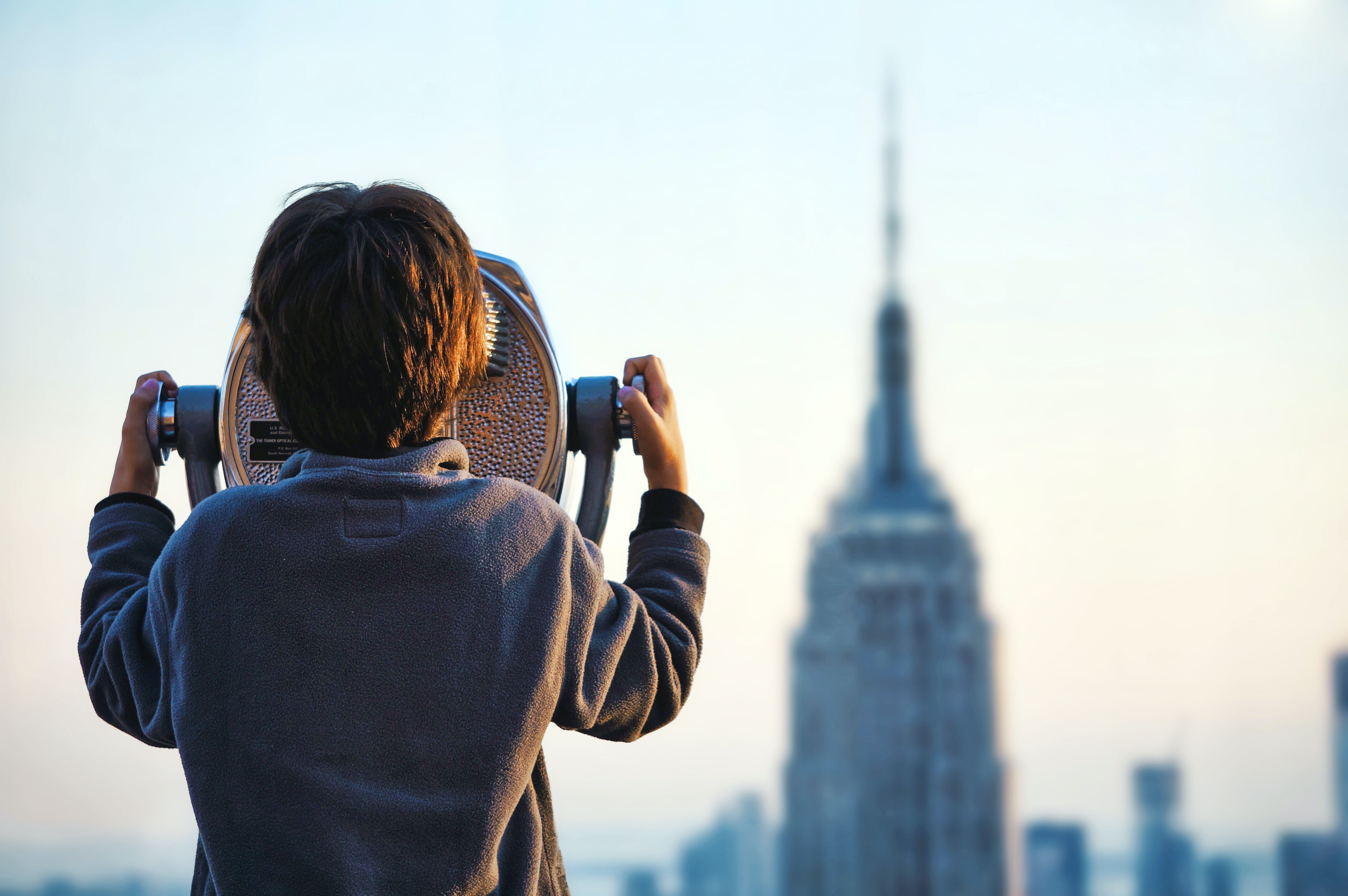 a child looks through a large telescope at the skyline of NYC