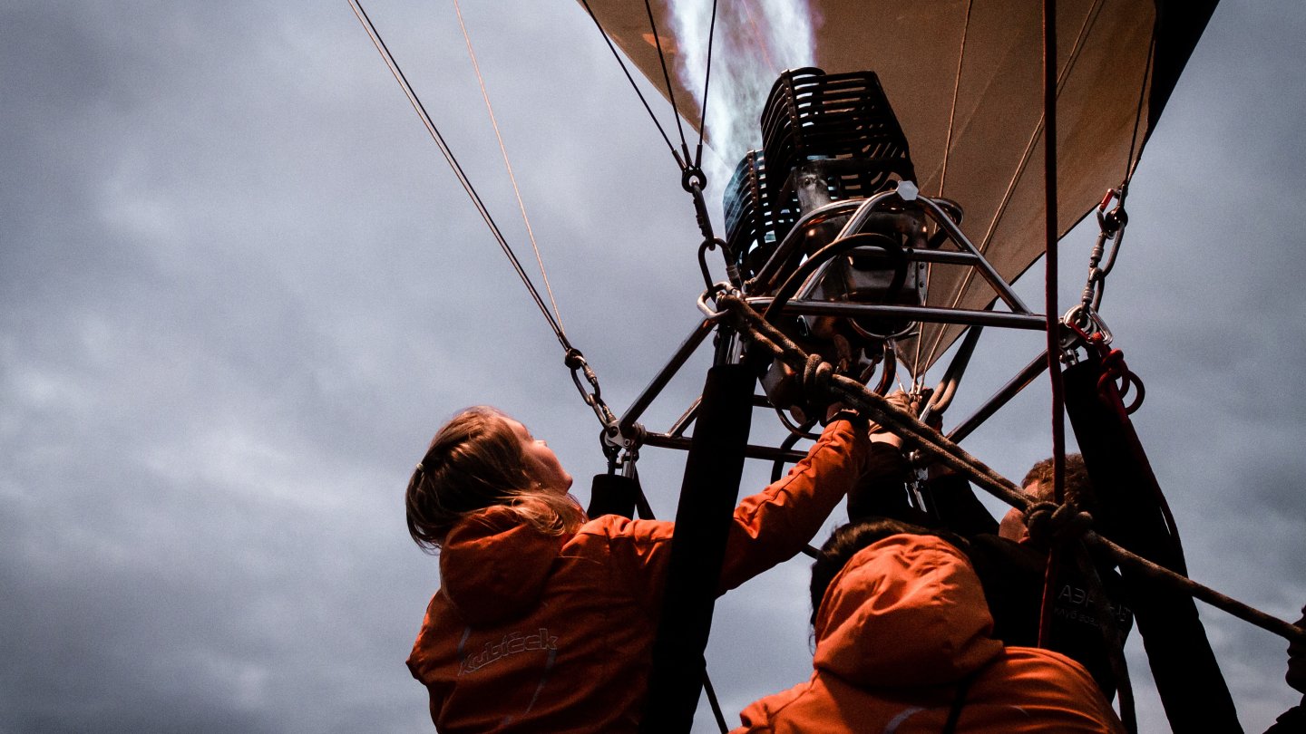 Das Bild zeigt zwei Menschen im Heißluftballon bei dem Anzünden des Gases.
